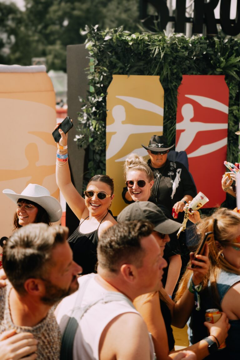 Two members of the PG team are smiling and having a good time at Brighton Pride at the Strongbow Yard, surrounded by other people.