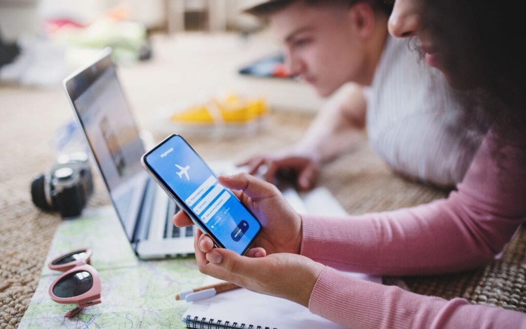 Two people lying on the floor, one on a laptop and one on a mobile planning a holiday