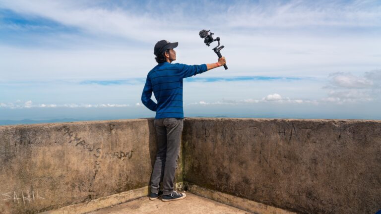 A person is holding a camera in front of them outside on top of a building and filming.