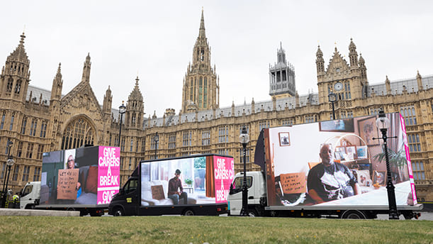 Set of 3 vans outsides the Houses of Parliament. Each one has a screen mounted to the back showcasing the Carers Trust campaign. People are being interviewed on the screens and text next to them says "Give Carers a Break."