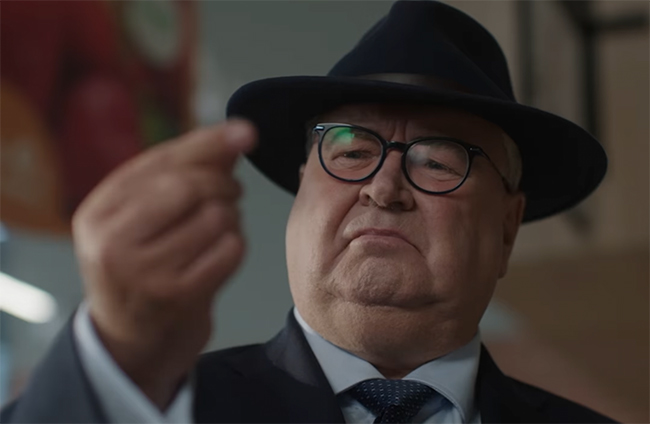 Joe Duffy in a crime noir suit inspects a blueberry at a Lidl store while figuring out whether or not their prices are too good to be true.