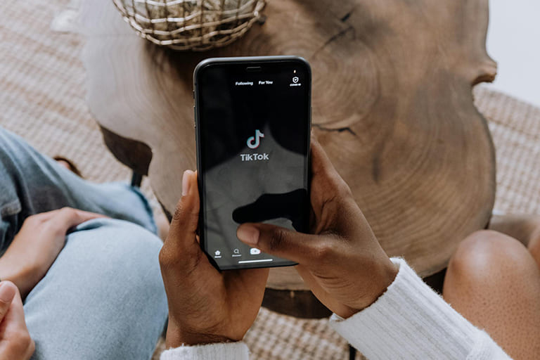 Person opening TikTok on their phone while sitting in a living room setting.