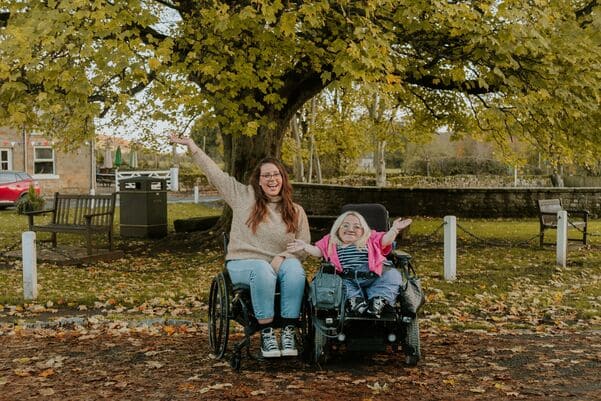Two girls in the park in wheelchairs smiling and celebrating together