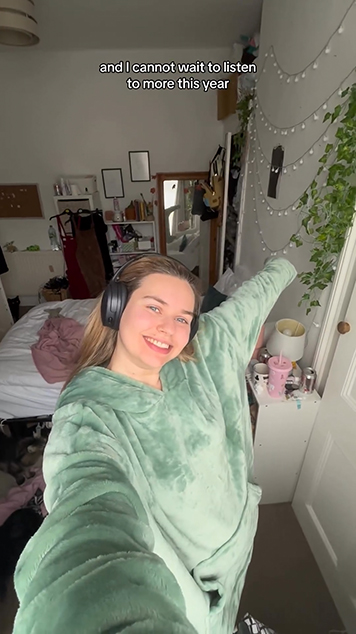 Ruby stands in her bedroom wearing headphones, she is listening to an audio book on Audible.