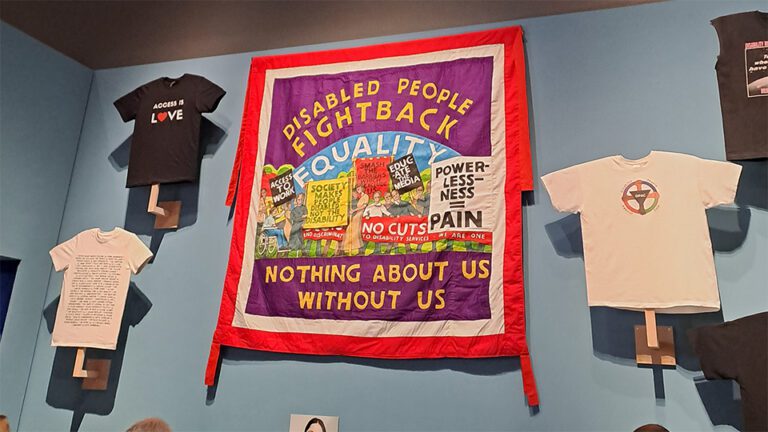 Set of t-shirts with pro-Disability Inclusion messages on them. In the centre of all of these is a large mural protesting against cuts to Disability Benefits. It has an illustration of people protesting and at the top and bottom are slogans including "Disabled people fight back," and "Nothing abut us without us."