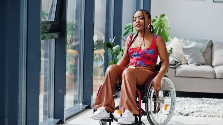 A female wheelchair user poses for a photo in from of a large window.