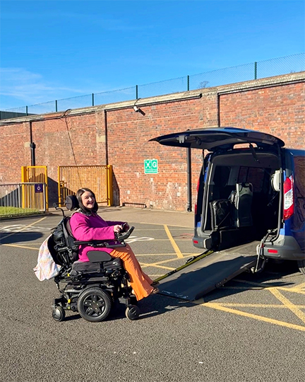 GM-Coachwork campaign image: A female powered wheelchair user is in front of the ramp leading into her Wheelchair Accessible Vehicle in an outside parking space.