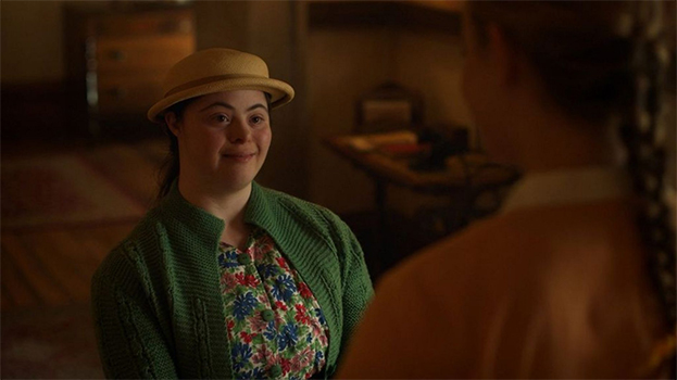 Frame from an episode of Malory Towers showing Ellie Goldstein, playing Nancy, smiling and talking to someone just out of focus on screen.