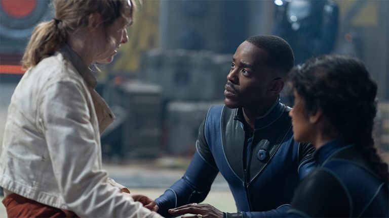 Doctor, Ncuti Gatwa, sits with companion Belinda, played by Varada Sethu, and Aliss, played by Rose Ayling-Ellis. The Doctor and Belinda comfort Aliss about the horrifying situation she finds herself in alone on an outer-space mining colony.
