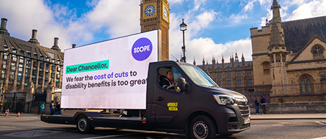 An advertising board is being driven around Westminster on the back of a van. Text from Scope reads: "Dear Chancellor, We fear the cost of cuts to disability benefits is too great."