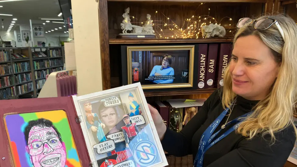 A woman holds up one of the books made by one of the contributing Disabled adults.
