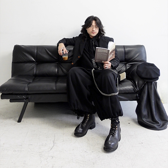 Person sitting on a leather sofa with a drink, reading a book. Their GUIDI shoes feature prominently in the foreground of the photo.
