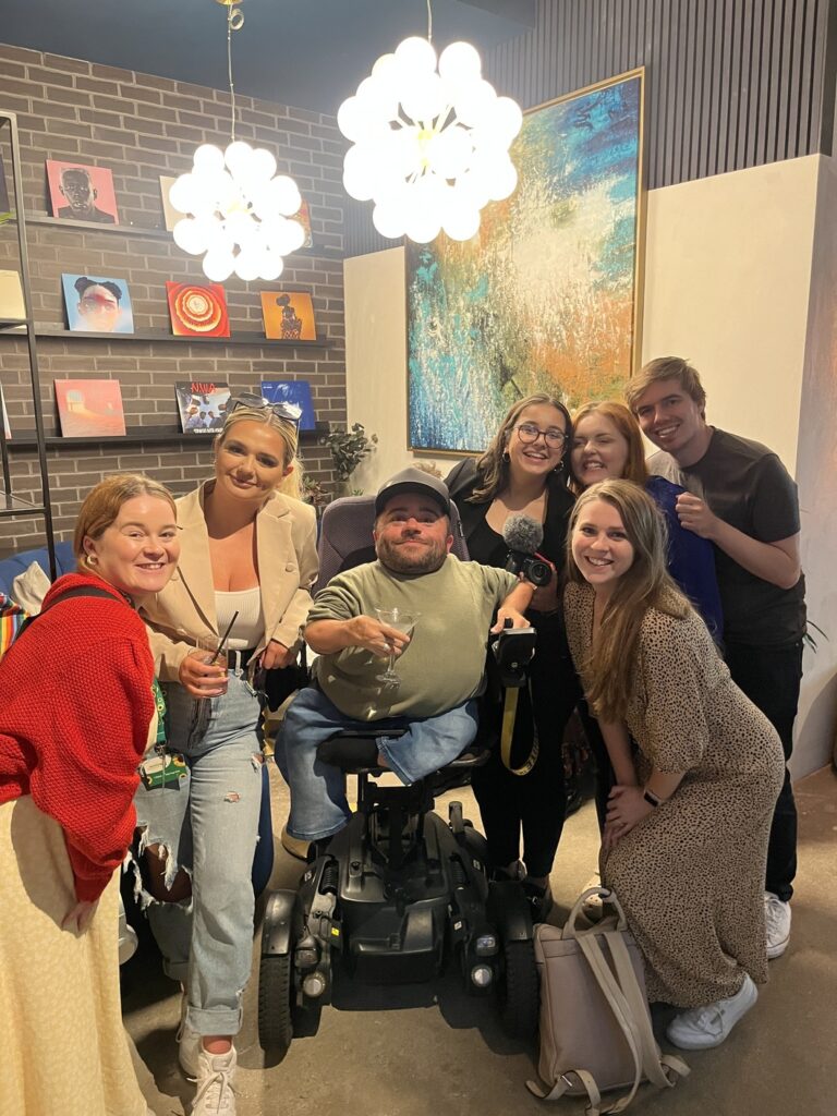 Some of The Purple Goat Team looking at the camera and smiling with friends of the agency. They are in a trendy, indoor setting filled with post-modern art.