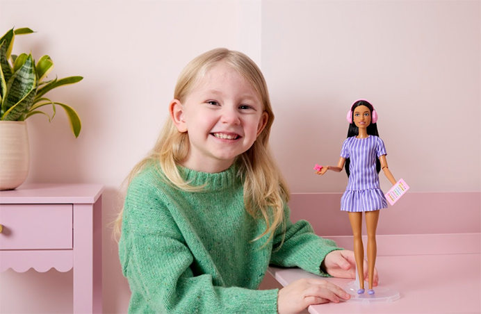 Little girl playing with the new Autistic Barbie, a Barbie Doll with noise-cancelling headphones and a fidget spinner among other indicators of Autistic lived experience.