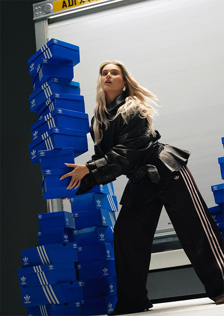 Molly Mae in Adidas branded clothing carrying a pile of Adidas shoe boxes.