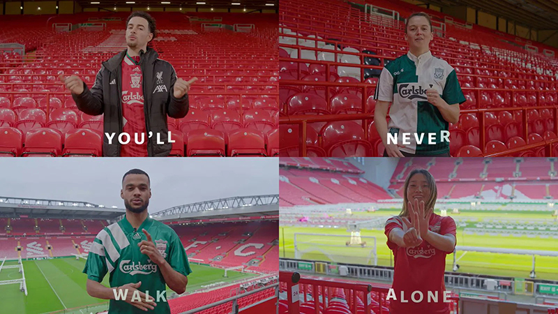 Four Liverpool football players signing the words for "You'll never walk alone," while wearing Carlsberg sponsored shirts.