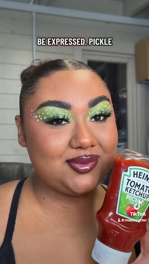 Miah poses with the new Heinz pickle ketchup flavour. She has applied bold, green eye makeup inspired by the flavour.