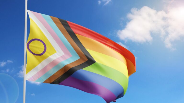 LGBTQIA+ flag flying against a sunny blue sky