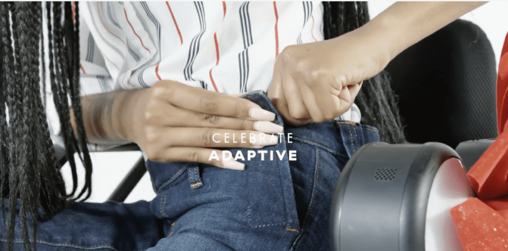A still image from the campaign with a black woman wearing some Tommy Hilfiger jeans from their adaptive collection. There is some text in the centre of the screen that says 'CELEBRATE ADAPTIVE'.