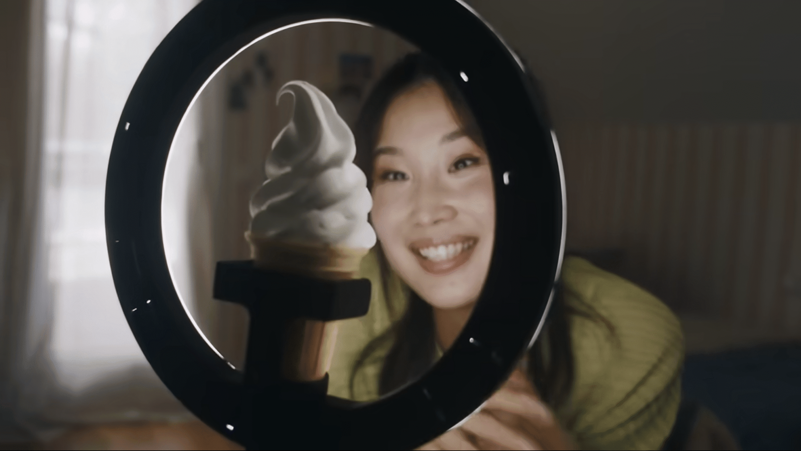 A woman is filming herself with a ring light in front of her, and a vanilla ice cream where her phone should be.