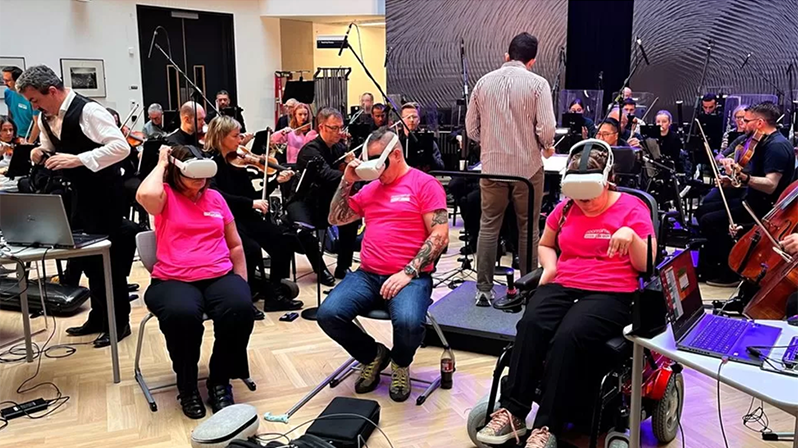 3 disabled artists wear some VR headsets while playing with the Ulster Orchestra behind them.