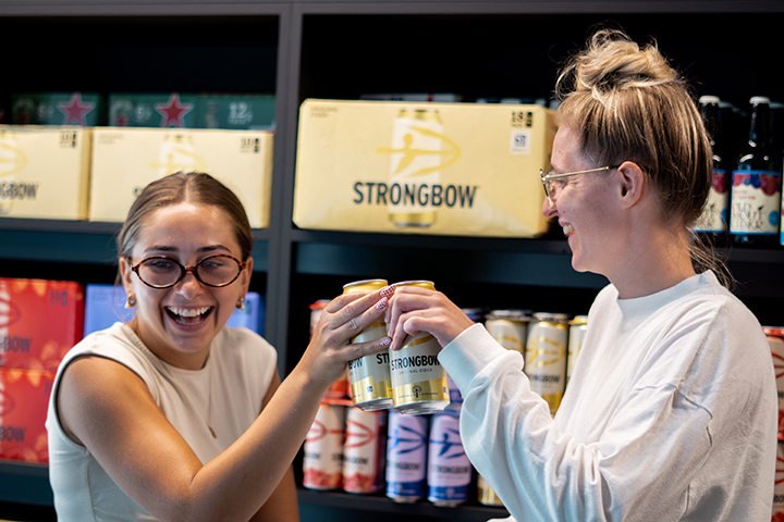 Two women do a cheers with two cans of Strongbow with the Navilens code on them.