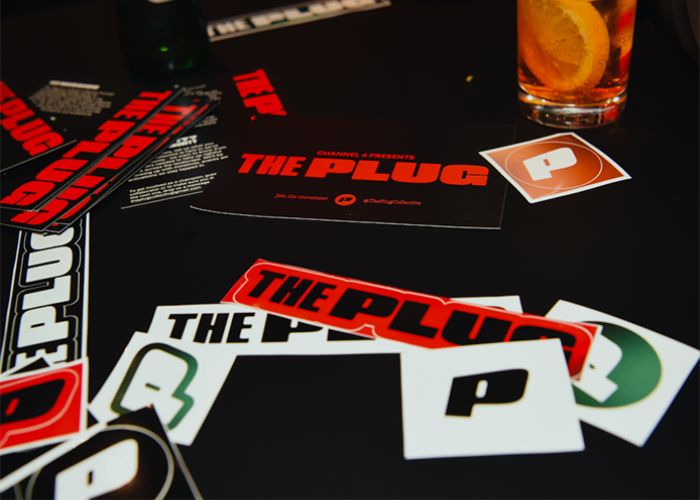Stickers with 'The Plug' logo on them, spread out on a black surface amongst party drinks.