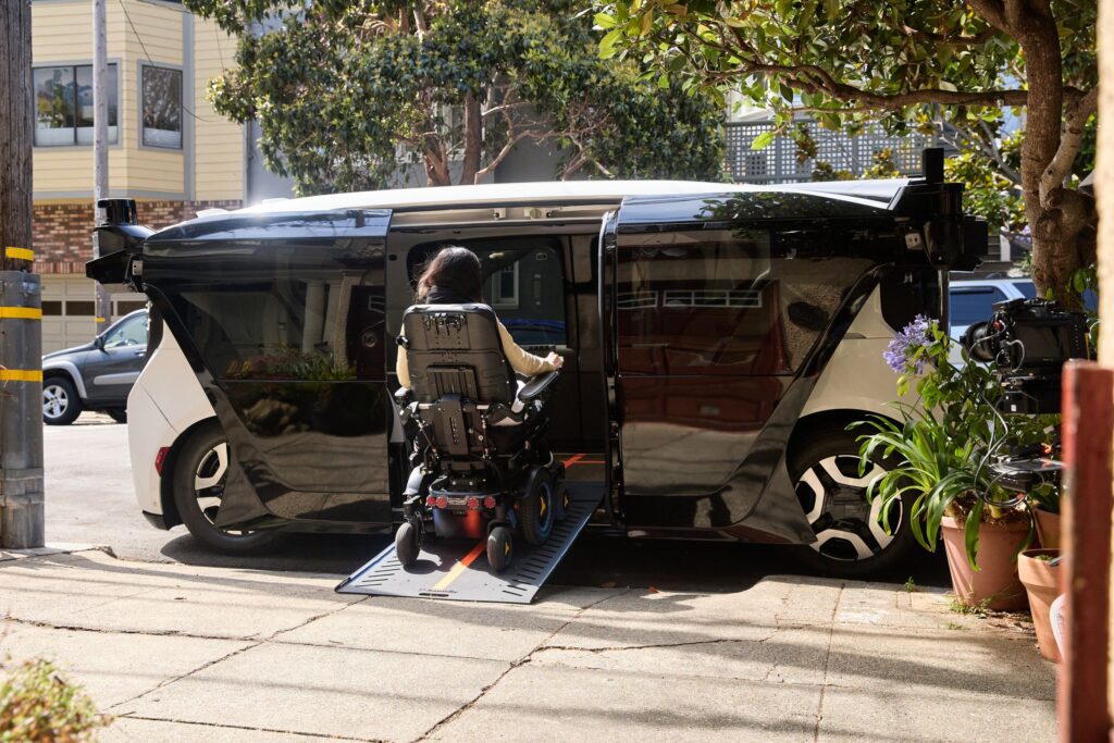A picture of a futuristic looking taxi, opening its doors to a wheelchair passenger, who is getting inside through a ramp.