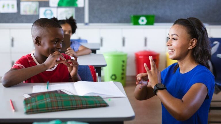 A school room where a student is learning sign language while looking at their teacher signing.