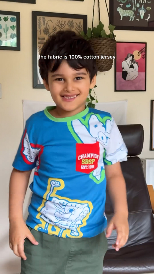 For Paramount campaign, a young boy stands in a living room smiling at the camera while wearing Spongebob adaptive wear. Caption on the screen reads: "the fabric is 100% cotton jersey."