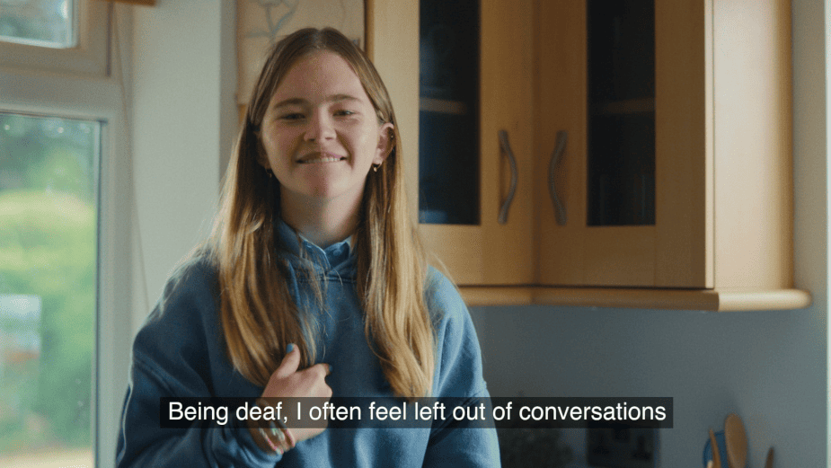 A young girl sits on the counter top in her home kitchen, signing to the camera. The caption reads: "Being deaf, I often feel left out of conversations."