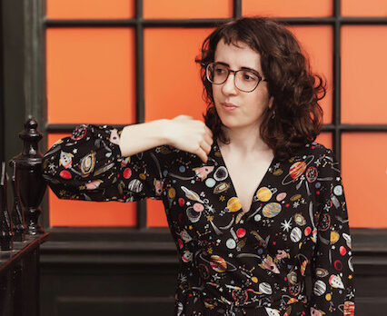 Lydia, a white brunette woman with some glasses and a floral dress, holding a walking aid.
