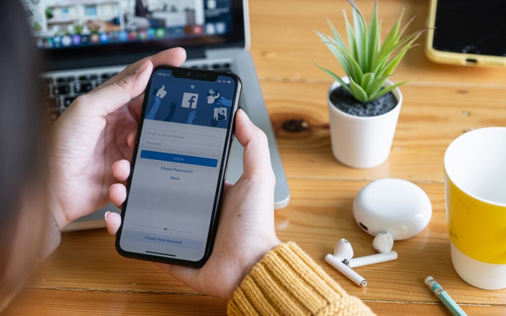 Lady sits at a table holding a phone with Facebook app open.