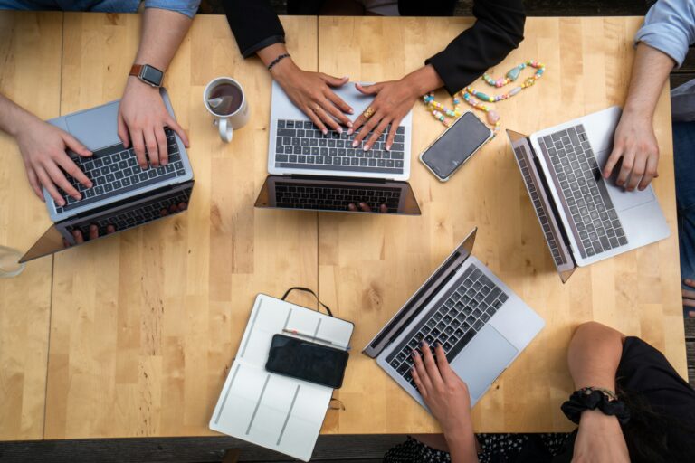 A group of people are working together around a table with their laptops.