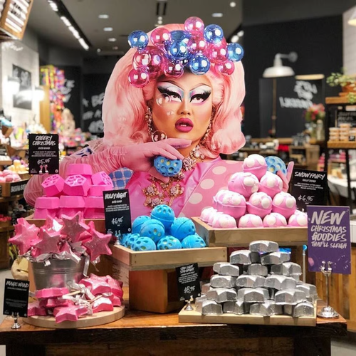 A drag queen is posing with some LUSH products.