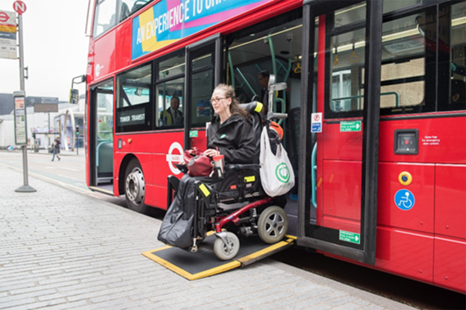 A person in a wheelchair leaves a red bus through its ramp.