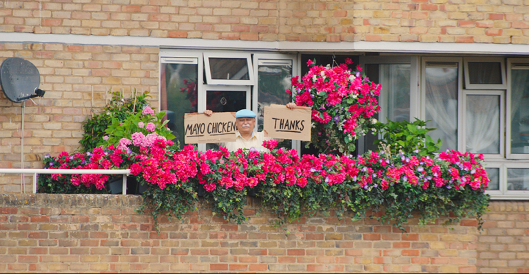 An image from the McDonald's ad 'McDelivery, You In?', showing an old man on his balcony full of pink flowers, holding two signs, one says 'MAYO CHICKEN', and the other one says 'THANKS'.
