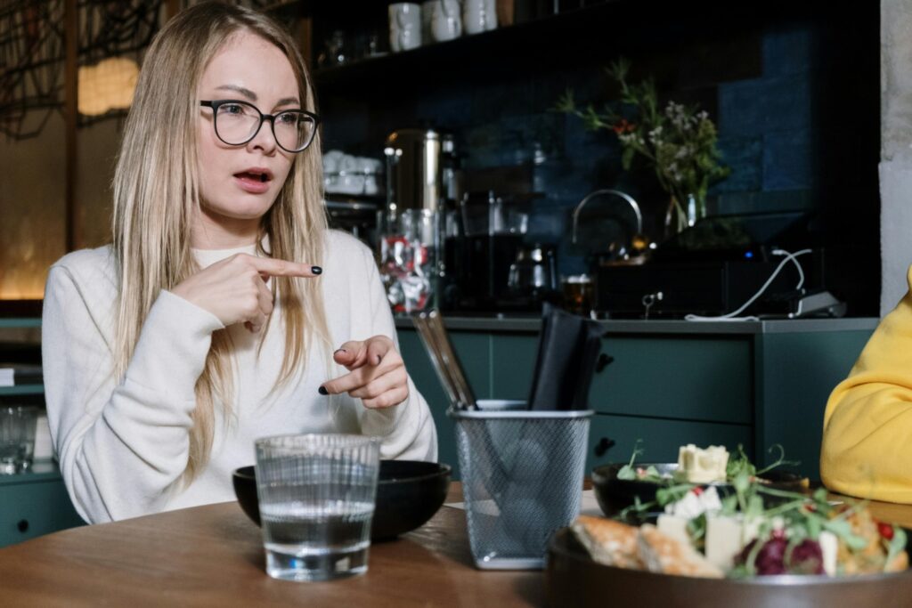 A woman is sitting at a table in a restaurant doing some sign language.