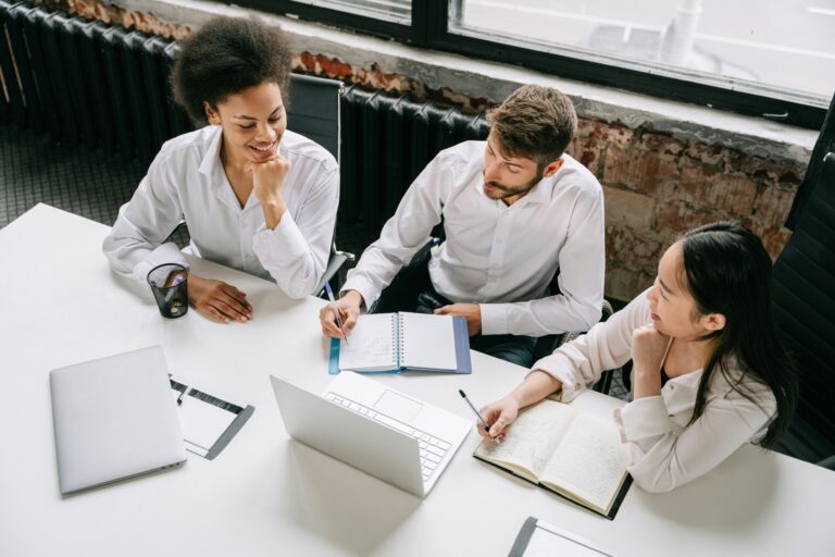 A diverse group of three people are sat around a white table at work.