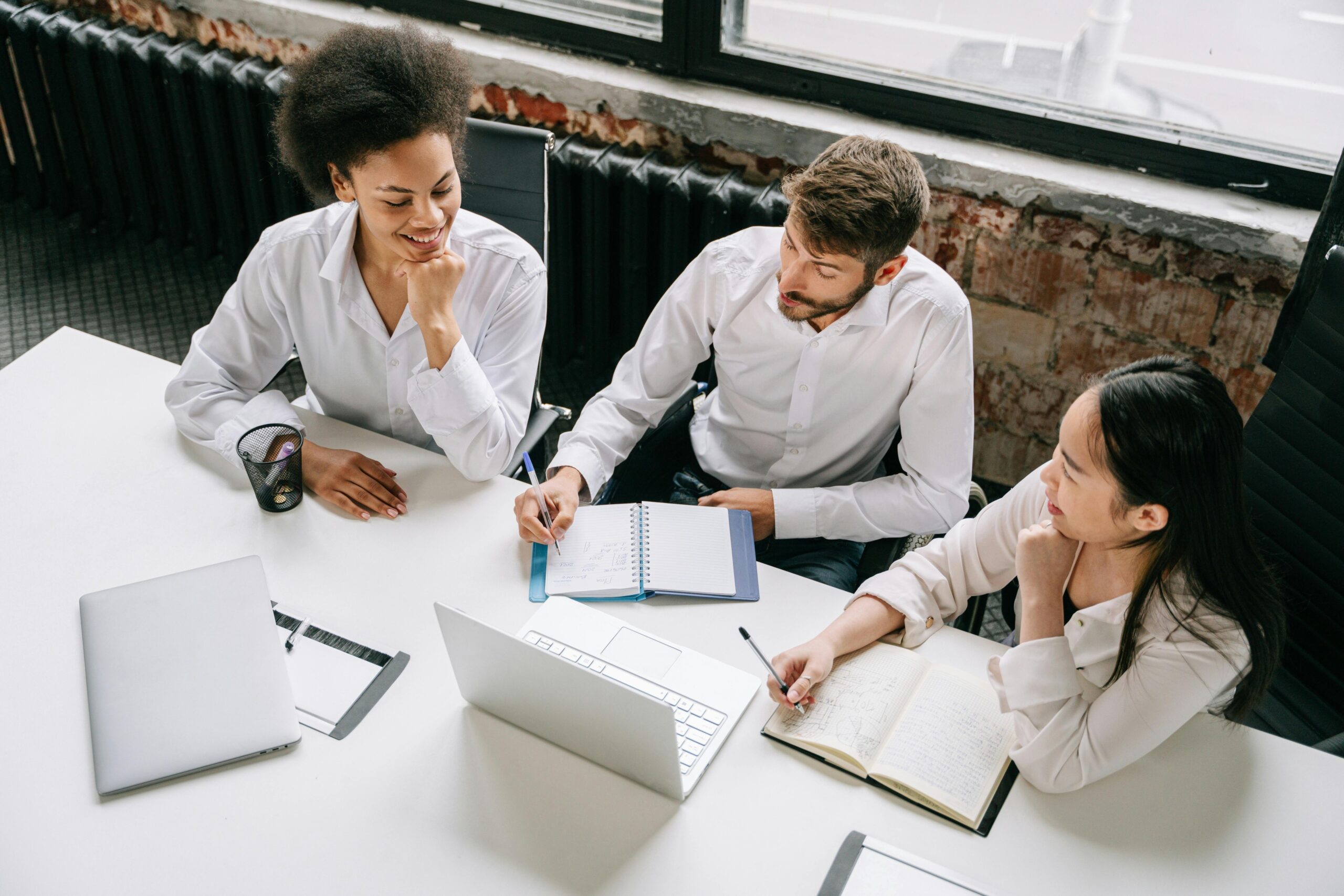 A diverse group of three people are sat around a white table at work.