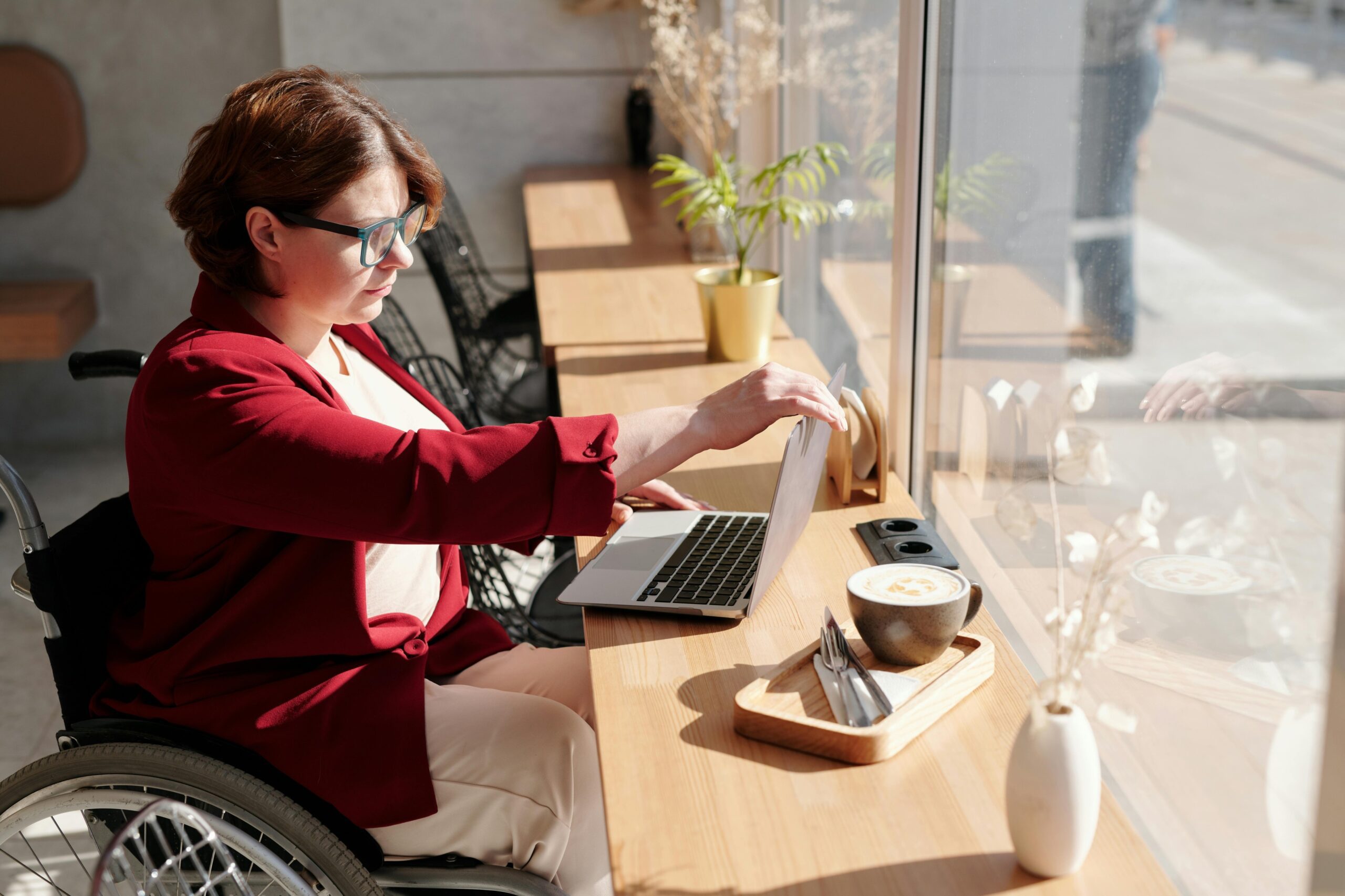 A woman in a wheelchair is in a cafe working on her laptop.