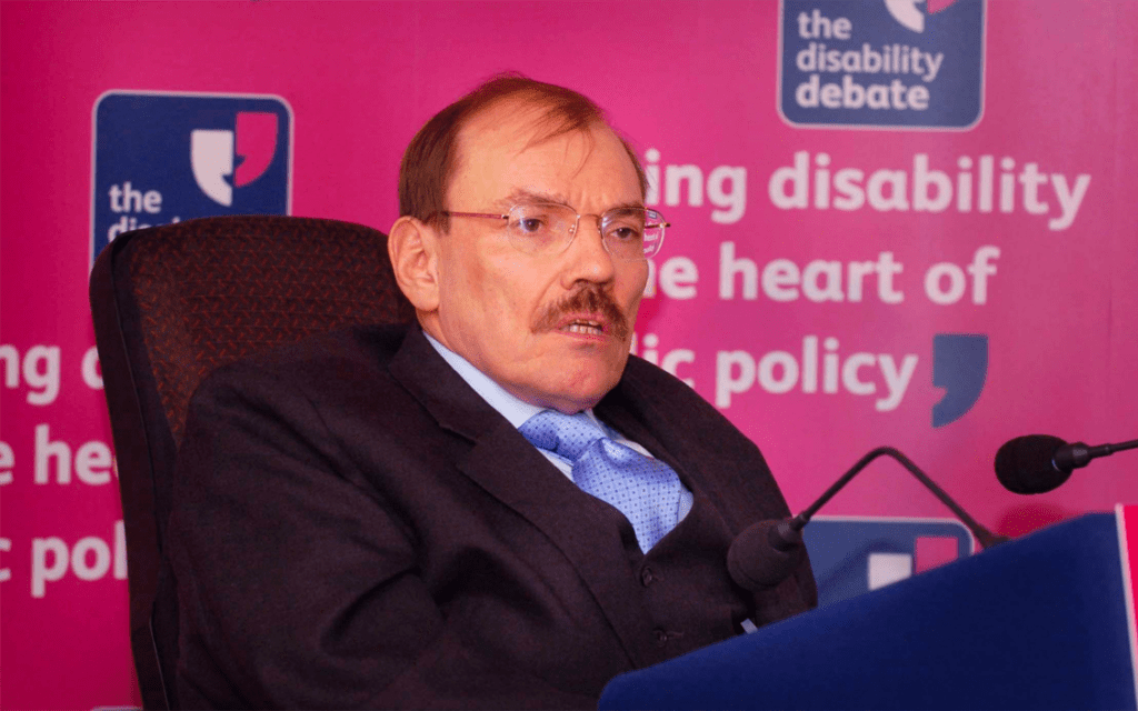 A picture of Sir Bert Massie, a white man with short brown hair and glasses, wearing a black suit.