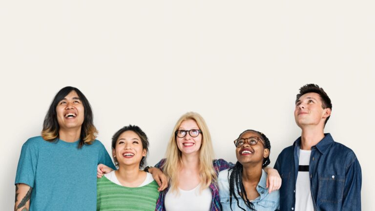 5 diverse people with their arms around each others shoulders, looking up and smiling.